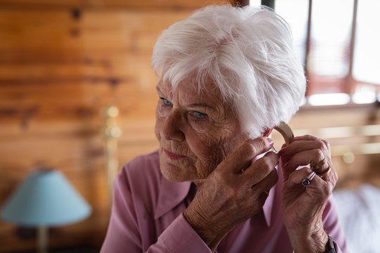 Active senior woman wearing a hearing aid in her ear in bedroom at home