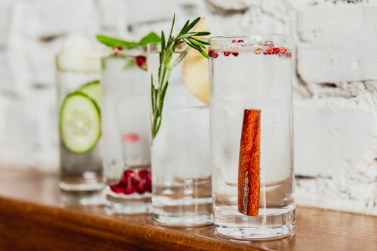 A horizontal image of 4 different refreshing gin and tonics in highball glasses. Cucumber and melon, pomegranate and basil, rosemary and apple, cinnamon and rose pepper. Selective focus.
