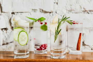 Fototapeta na wymiar A horizontal image of 4 different refreshing gin and tonics in highball glasses. Cucumber and melon, pomegranate and basil, rosemary and apple, cinnamon and rose pepper. Selective focus.
