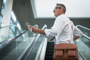 Businessman checking his mobile phone on the escalator