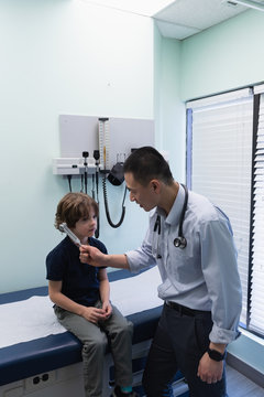 Young asian male doctor showing tuning fork to caucasian boy patient in clinic 
