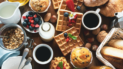 Obraz na płótnie Canvas Health and colorful breakfast - cups of coffee with granola, waffles, muffins,almond,hazelnuts,various fresh fruits, berries and milk on old wooden table. Health food concept .Top view.