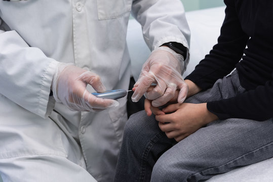 Young asian male doctor examining caucasian boy patient with glucometer in clinic 