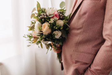 the groom holds a wedding bouquet in his hands