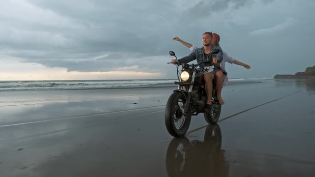 Young beautiful couple hipsters riding retro motorcycle on the beach, outdoor portrait, riding guy and girl, travel together, ocean, sea