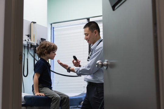 Young asian male doctor examining a caucasian boy patient with medical tool 