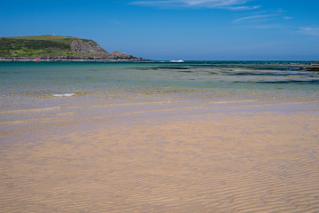 A quiet sunny day at Daymer Bay, Trevetherick in North Cornwall, UK with shallow waves lapping a sandy beach 