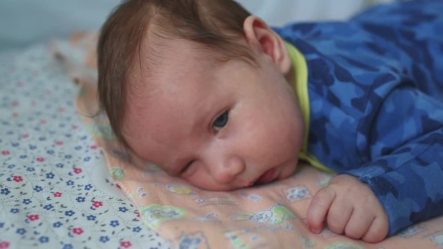 infant lies on his stomach with big eyes open on a bed for newborns.