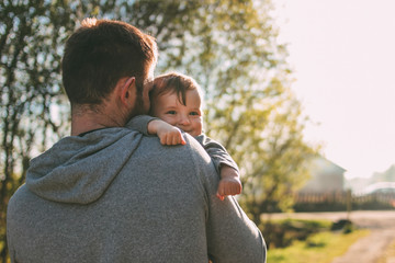 Cute baby boy on his dad's shoulders walking on the village road outdoors, sensitivity to nature...