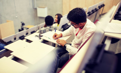 education, high school, university, learning and people concept - group of international students with notebooks writing in lecture hall