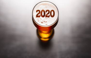 New Year beer. 2020 symbol on beer glass foam on black table, view from above