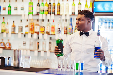 African american bartender at bar making coctails on shots. Alcoholic beverage preparation.