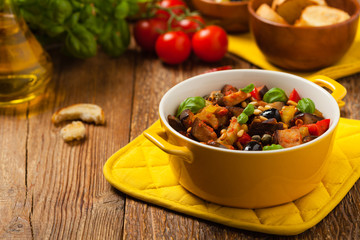 Traditional Italian caponata, served with croutons in a yellow, sunny pot. Decorated with basil and pine nuts.