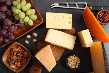 Different types of cheese on a wooden board and other snacks like nuts, fruits. - 269986772