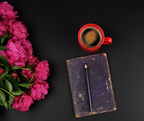 red creameric cup with black coffee, closed notebook and a bouquet of red peonies