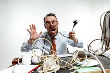 Completely confused. There are a lot of wires in the workplace and man is constantly tangled in them. It's literally blocking him. Concept of office worker's troubles, business, problems and stress.