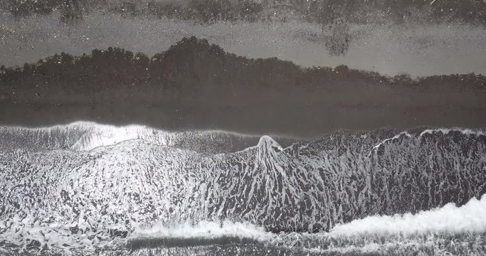 Top down aerial view of waves on black sand beach in Amed, Bali, Indonesia