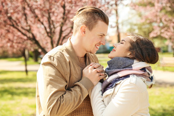 Fototapeta premium Happy young couple holding hands and smiling in spring park with blooming trees, romantic relationship and dating, the man and woman are looking at each other with affection