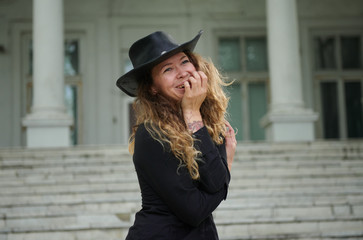 fashionable girl dressed in black shirt, hat and wide trousers posing near old white house