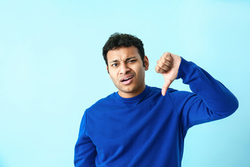 Displeased man showing thumb-down on color background