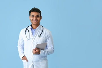Handsome doctor with tablet computer on color background