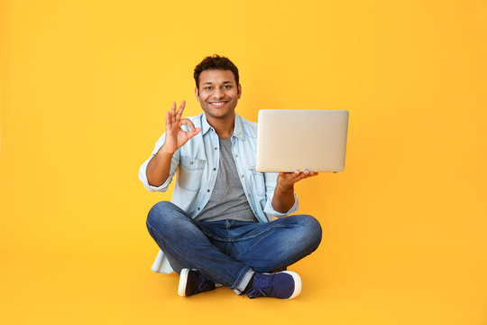 Handsome man with laptop showing OK on color background