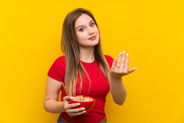 Young teenager girl holding a bowl of cereals inviting to come with hand. Happy that you came