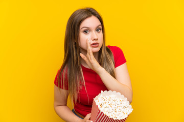 Young woman with popcorns over pink wall whispering something