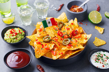 Nachos chips with Mexican flag and dips variety in black bowl. Grey stone background.