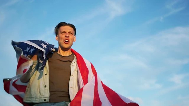 Celebration of US Independence Day. A man screams and slaps his chest. Holds the flag of the United States