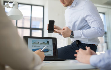 business, people and technology concept - close up of businessman showing smartphone to colleagues at office