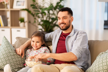 family, fatherhood and people concept - happy father and daughter with popcorn watching tv at home