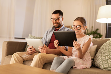 family, fatherhood and technology concept - happy father and daughter in glasses with tablet pc computers at home