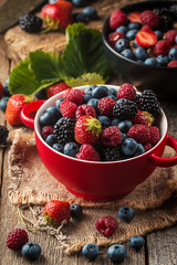 Ripe sweet different berries in red bowl on rustic wooden table. Harvest Concept