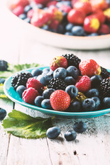 Ripe sweet different berries in a blue bowl on white wooden table. Harvest Concept