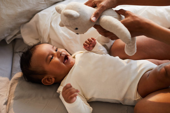Close-up of mother showing toy bear to black baby boy lying on bed and having fun from game