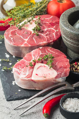 Fresh veal shank slices beef meat for Osso Buco cooking on cutting board with ingredients and seasonings thyme, pepper, salt.
