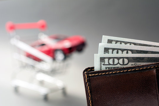 Leather Wallet With Dollars Blurred Red Car Shopping Trolley On The Background. Cheap Used Cars Concept