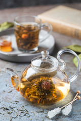 Hot green tea drink. Teapot and glass cup with blooming tea flower inside against stone background