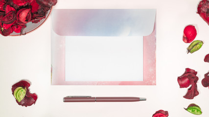 Blank open letter on envelope on a desk with writing supplies and pink dried flowers