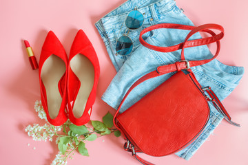 Flat lay feminini clothes and accessories collage with blue (fit mom) jeans, sunglasses, small red handbag, lipstick, vermeil high heel shoes, on pastel pink background. Womans trendy fashion clothes.