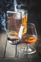 Glass and a bottle of brandy or cognac and smoking cigar on the wooden table.