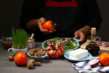 Chef hands cooking Seasonal salad. Persimmon, avocado, pomegranate and different lettuce leaves