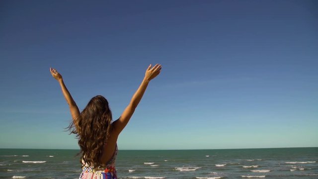 Woman in summer dress rising her hands. Canoa Quebrada beach in background