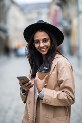 Young pretty woman with coffee to go standing at the street and using mobile phone