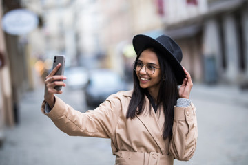 Portrait of wonderful lovely woman in stylish hat making selfie while walking on the street.