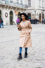 Portrait of happy woman in black hat walking with coffee to go on a city street