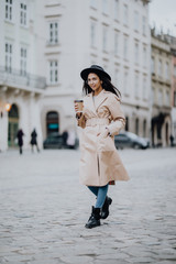 Coffee on the go. Beautiful young woman holding coffee cup and smiling while walking along the street