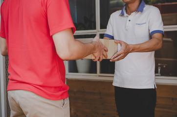 smart home delivery service man in red uniform handing parcel boxes to recipient and young man customer accepting parcel post box from courier at home, express delivery and online shopping concept