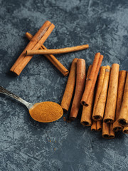 Ground cinnamon in a spoon and cinnamon pods on a dark background